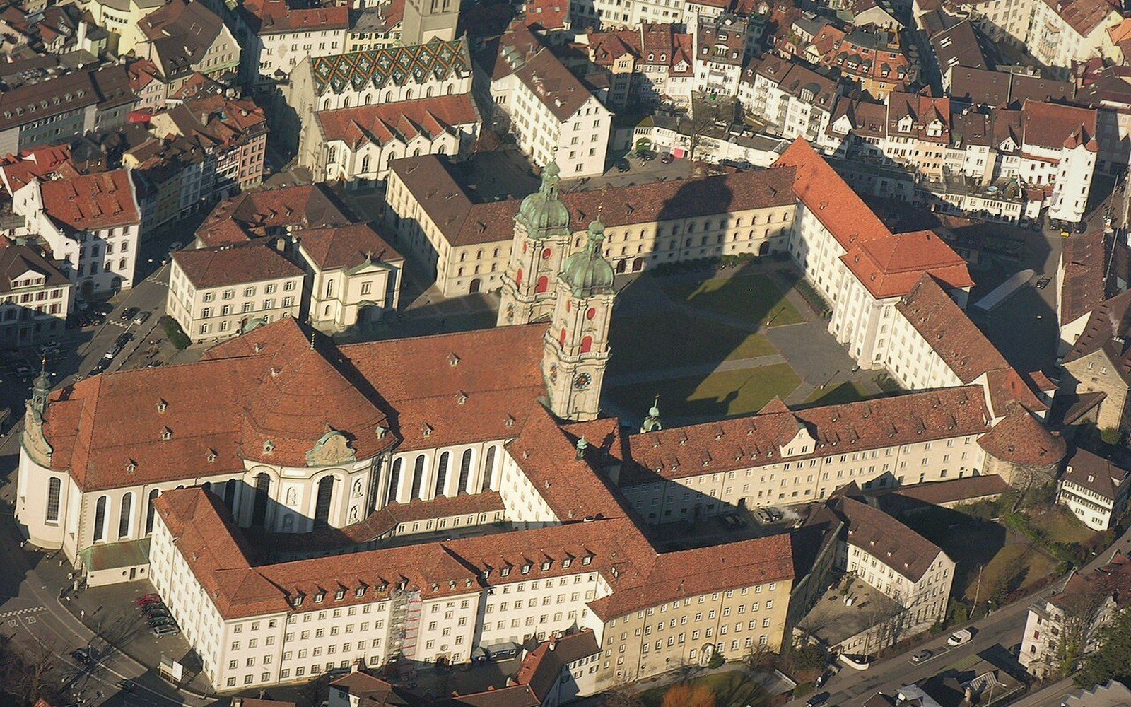 Aerial view of a twin-towered abbey cathedral surrounded by dense city rooftops