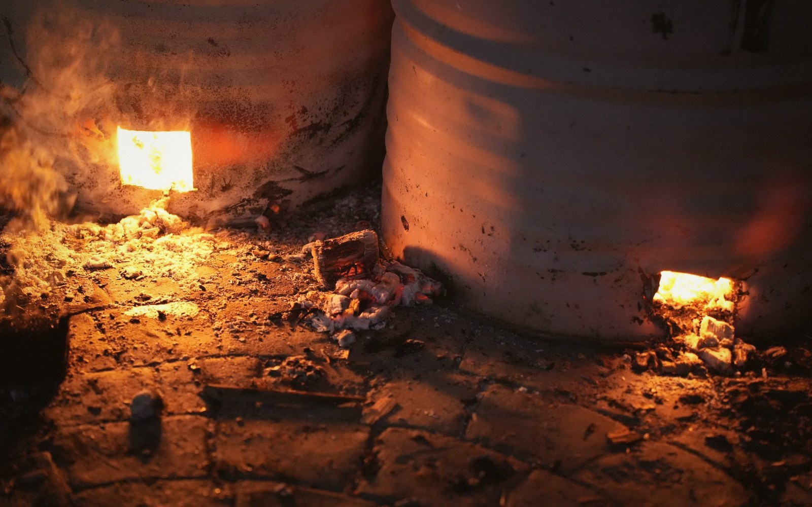 Glowing embers burn beneath large metal drums used in a malting kiln