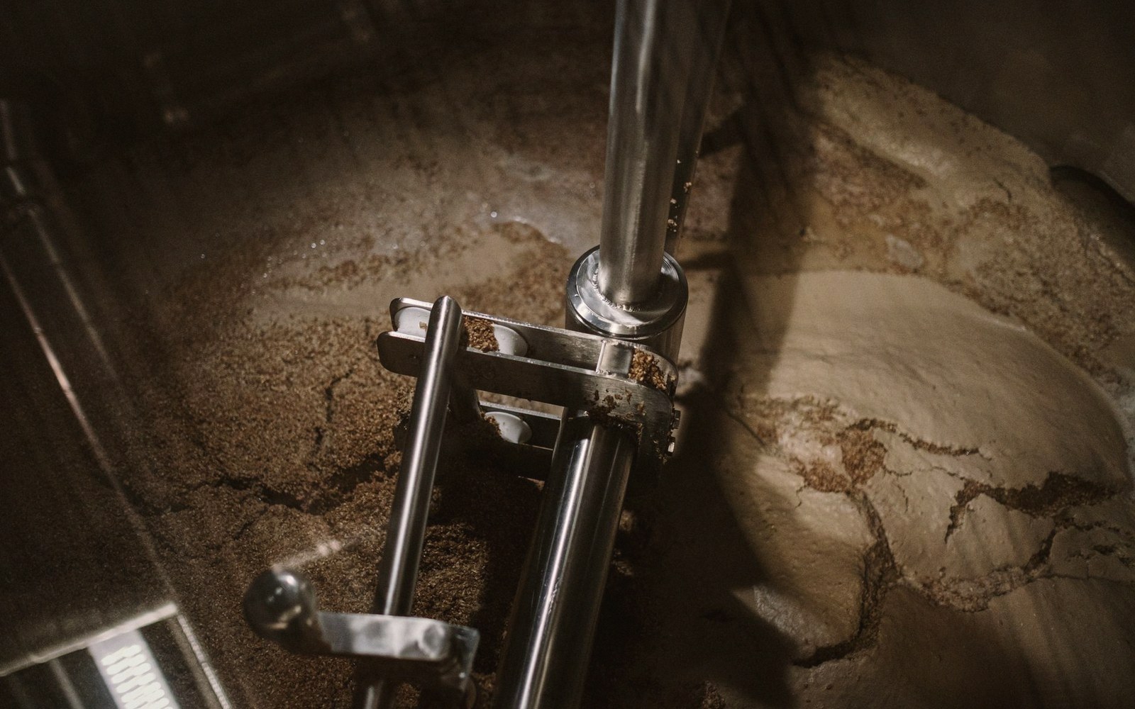 Steel rake arm and central shaft inside a mash tun filled with grain