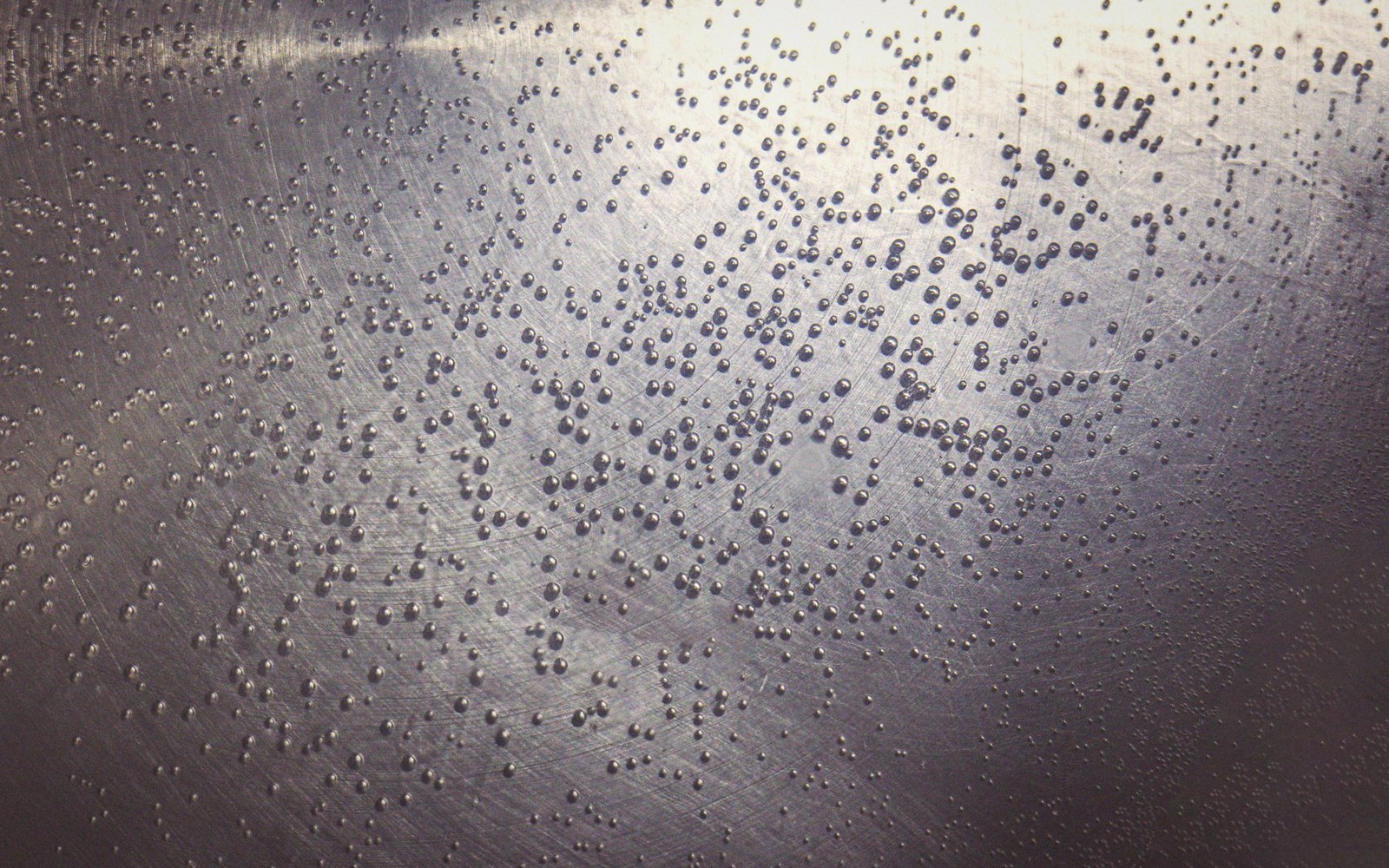Water droplets scattered across a scratched metal surface reflecting light