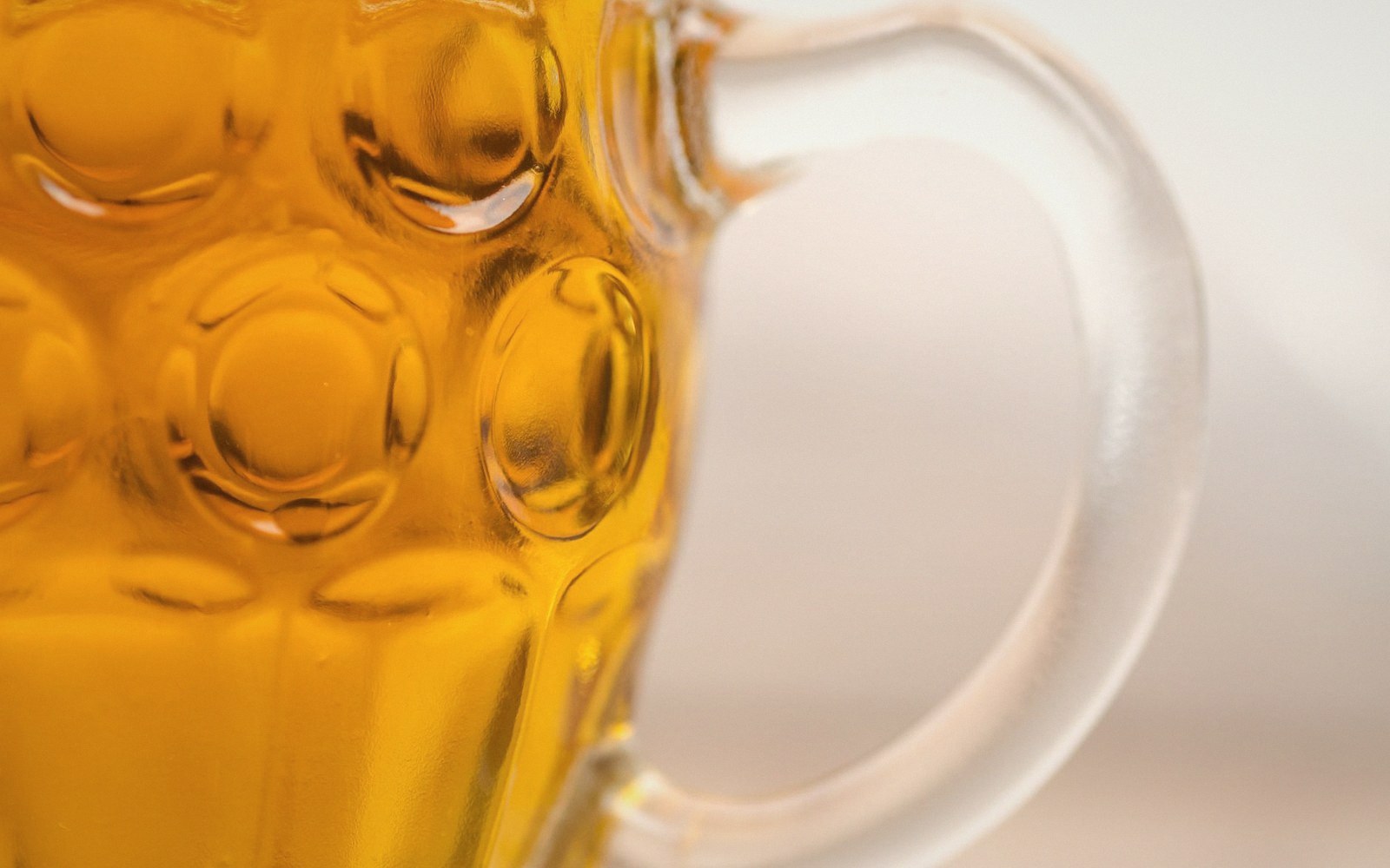 A filled glass of amber beer held against a leaded window, backlit, condensation on the outside